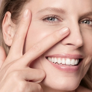 A person places two fingers around their eye, smiling in a close-up shot, emphasizing skincare.