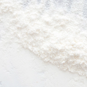 Powder spreads across a surface, creating a textured, fluffy white layer, illustrating a skincare product ingredient's appearance and consistency.