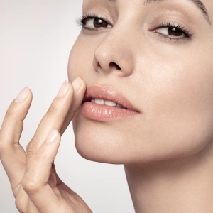 A woman gently touches her lips with fingertips, displaying smooth, clear skin in a promotional context for dermatological face and body care.